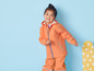 Une fille porte un imperméable et un pantalon orange.