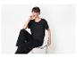Femme en t-shirt noir et pantalon large, assise sur une chaise transparente, souriante.