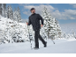 Homme en veste et pantalon d'hiver noirs marchant dans la neige avec des bâtons de randonnée.