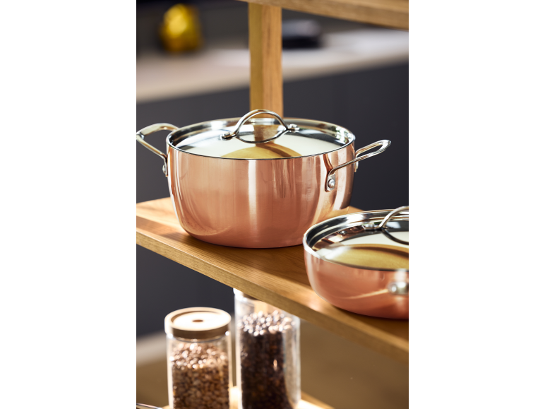 Casseroles et poêles en cuivre sur une étagère en bois dans la cuisine.