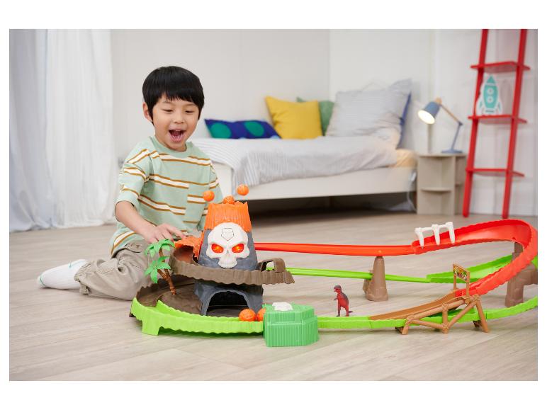 Garçon heureux joue avec un circuit de course sur le thème des dinosaures avec un volcan.