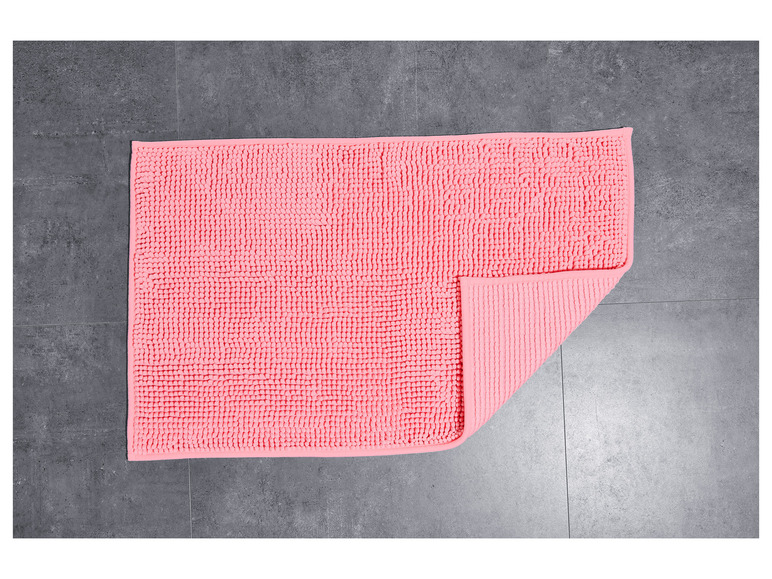 Un tapis de bain rose avec une texture rugueuse, posé sur un carrelage gris.