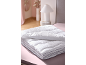 Couette blanche pliée sur un drap rose, avec lampe et décoration en arrière-plan.