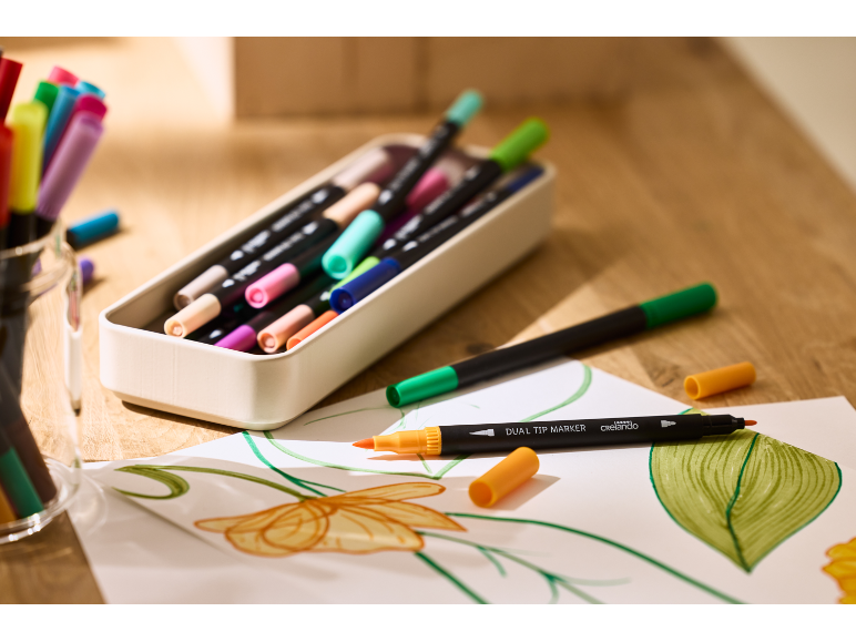 Marqueurs double pointe colorés et dessins sur une table en bois.