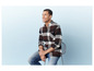 Homme en chemise à carreaux et en jean assis sur une chaise.