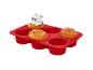 Moule de cuisson rouge en silicone à six cavités, dont trois contiennent des muffins, un avec un glaçage vert clair.