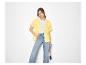 Femme en chemise jaune, t-shirt blanc et jean large, avec un sac en paille.