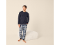 Homme en pyjama bleu marine et pantalon à carreaux, souriant.