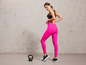 Une femme en leggings roses et chaussures de sport noires avec un kettlebell au sol