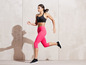 Une femme en leggings de sport roses et un soutien-gorge de sport noir court pendant un entraînement.