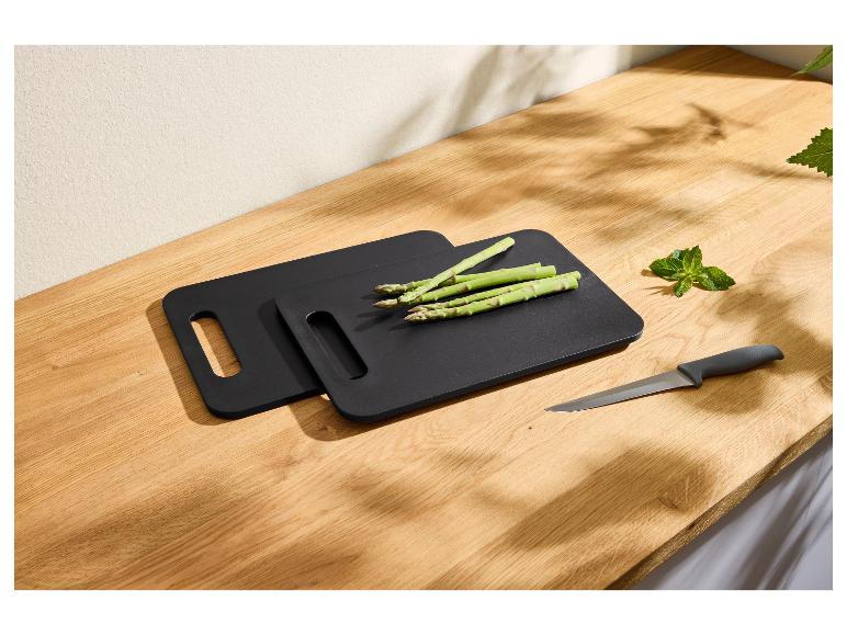 Planches à découper noires avec asperges, un couteau et de la menthe sur une surface en bois.