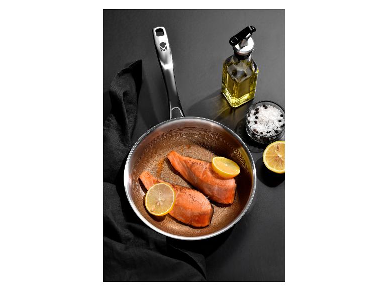 Poêle avec deux filets de saumon, citron, sel et poivre sur fond noir.