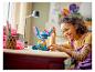 Une fille souriante joue avec une grande figurine Stitch en briques LEGO sur une table.