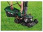 Personne fixant un bac de ramassage d'herbe à une tondeuse à essence Parkside sur l'herbe verte.