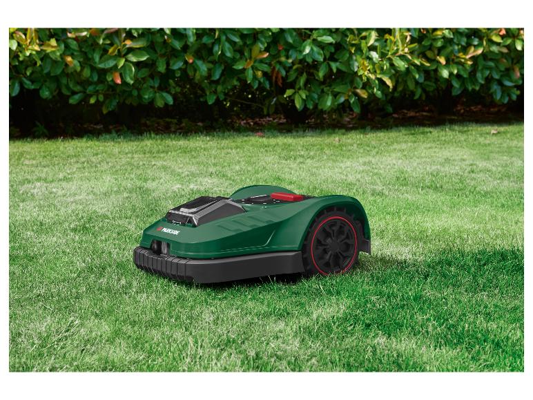 Tondeuse robot verte Parkside sur une pelouse devant des buissons.
