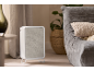 Purificateur d'air blanc avec panneau frontal en tissu gris clair dans un salon.