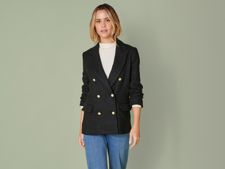Une femme portant un blazer noir avec des boutons dorés et un jean bleu.
