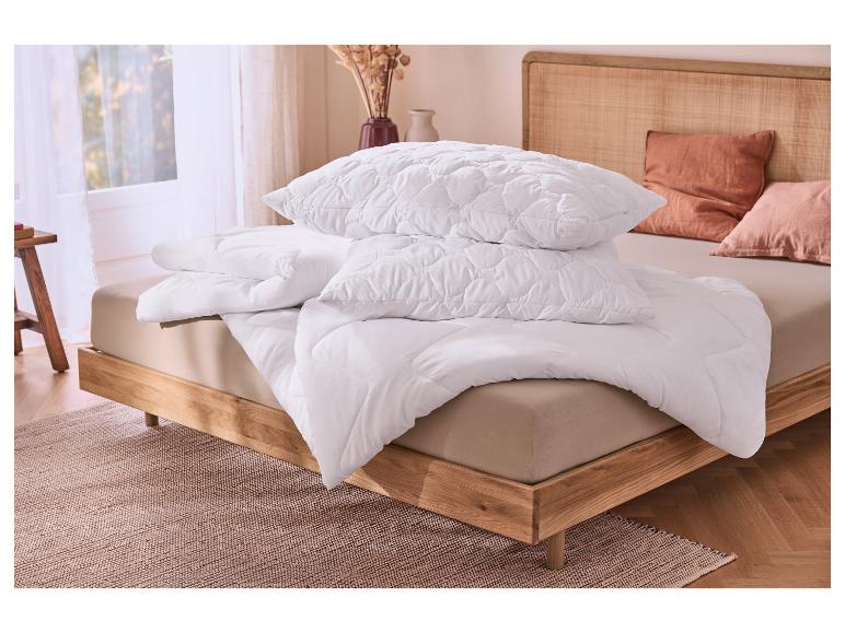 Couette et oreillers blancs sur un lit en bois avec literie beige dans une chambre.