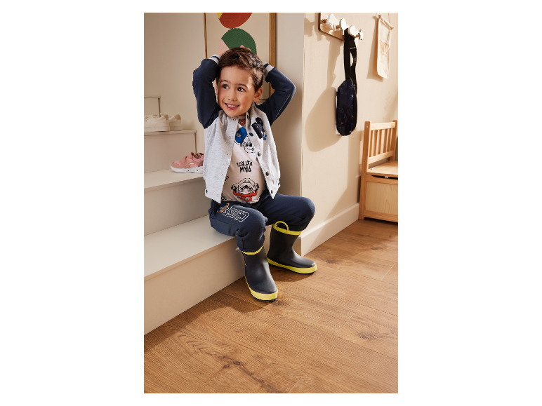 Petit garçon assis sur une marche d'escalier avec des vêtements et des bottes de pluie Paw Patrol.