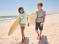 Deux enfants marchent sur la plage avec des planches de surf.