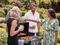 Des amis font griller du maïs, des tomates et des brochettes sur un barbecue à gaz dans le jardin.