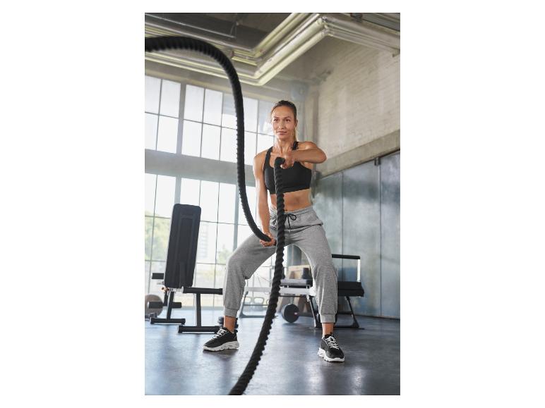 Femme en tenue de sport utilisant des cordes de combat dans une salle de sport.
