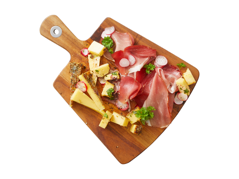 Planche en bois avec charcuterie, fromages, radis et persil.