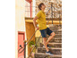 Homme en polo jaune, short en jean bleu et baskets bleues sur des marches en pierre.