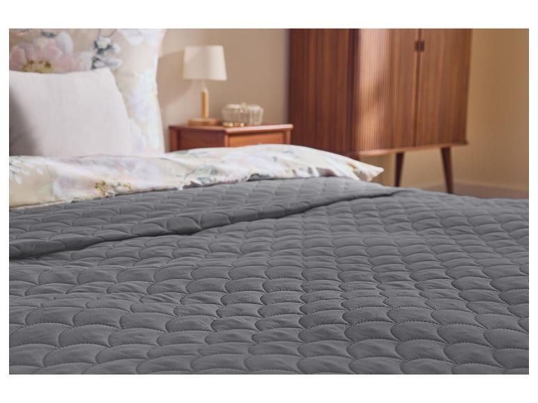 Couverture matelassée grise sur un lit avec parure de lit florale et table de chevet