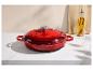 Cocotte en fonte rouge sur un comptoir en marbre blanc avec une bouteille d'huile et une planche à découper.