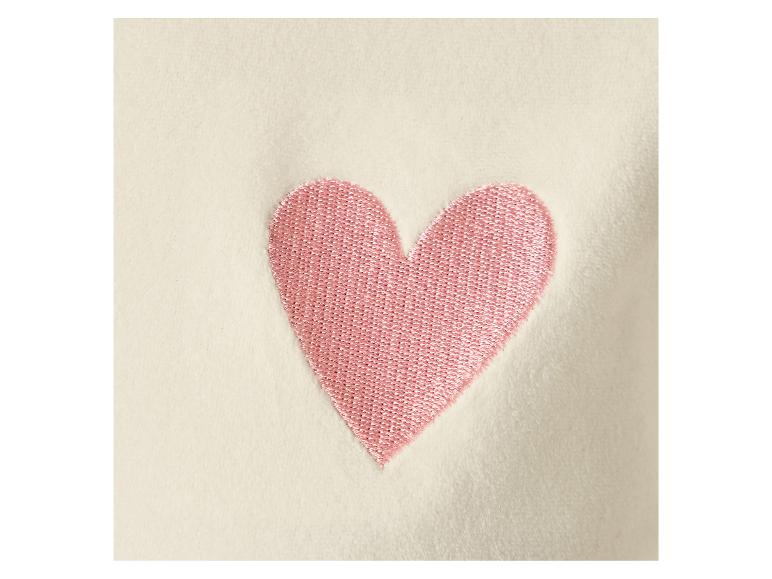 Gros plan d'un cœur rose brodé sur un tissu crème.
