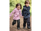 Deux enfants en pantalons et vestes softshell noirs avec des imprimés robots et animaux marchent main dans la main.