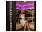 Femme en serviette blanche assise dans un sauna infrarouge avec éclairage violet.