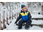 Enfant souriant en veste de ski et pantalon de neige assis sur des marches enneigées.