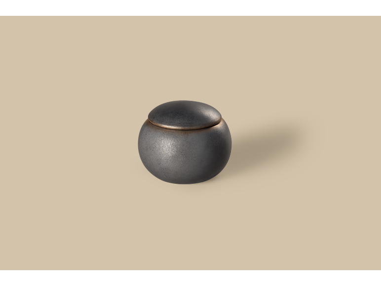 Urne funéraire sphérique en métal foncé avec couvercle, sur fond beige.