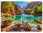 Nourriture et boissons sur une table près d'un lac turquoise avec une cascade et des falaises rouges.