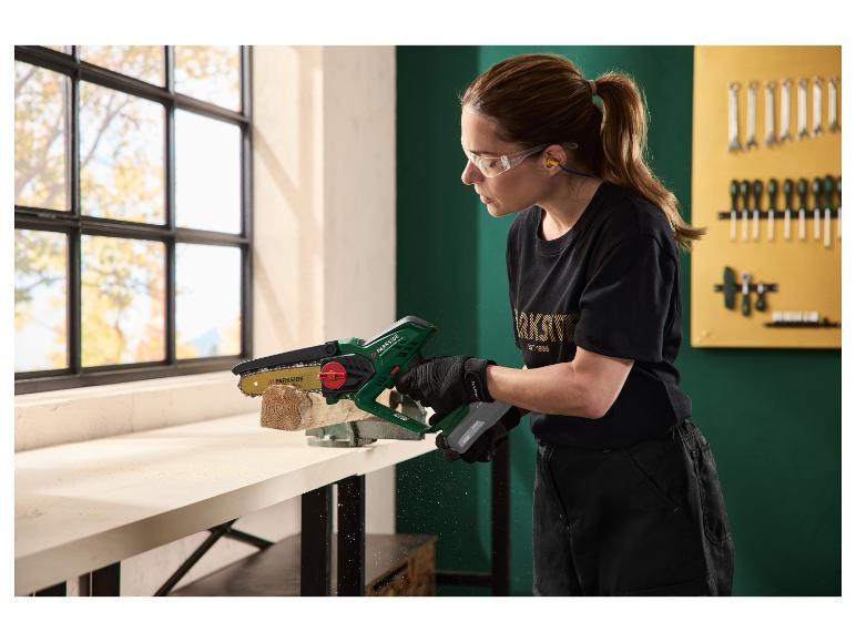 Femme coupant un morceau de bois avec une mini tronçonneuse, portant des lunettes et des bouchons d'oreille.