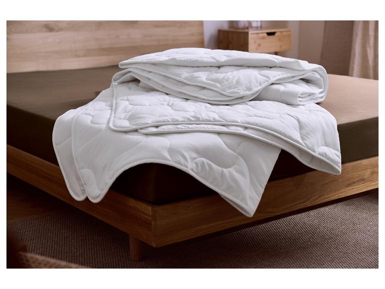 Couette blanche matelassée à motif ondulé sur un lit avec cadre en bois et drap marron.