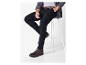 Un homme assis sur un tabouret blanc portant un pantalon noir et des chaussures brunes.