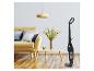 Aspirateur balai noir dans un salon moderne avec canapé jaune et table basse en bois.