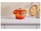 Casseroles empilées en fonte orange-rouge sur un comptoir avec des ustensiles de cuisine en bois.