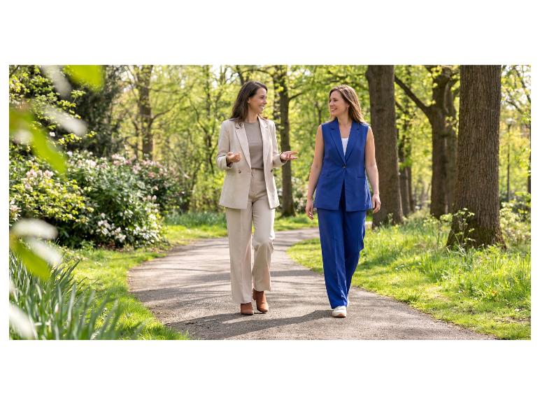 Deux femmes en costumes élégants marchent et sourient dans un parc.