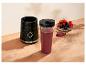 Base de mixeur noire avec une tasse de smoothie et un bol de baies fraîches sur une surface en bois.