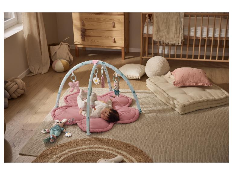 Bébé sur tapis de jeu rose avec arche d'activités, dans une chambre d'enfant.
