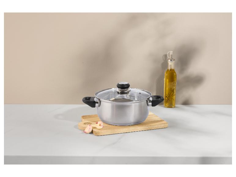 Casserole en acier inoxydable avec couvercle en verre, ail et bouteille d'huile d'olive sur un comptoir.