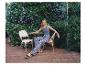 Femme en débardeur bleu et pantalon à motifs assise sur une terrasse verdoyante.