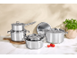 Ensemble de casseroles et poêles brillantes en acier inoxydable sur un comptoir avec herbes et tomates.
