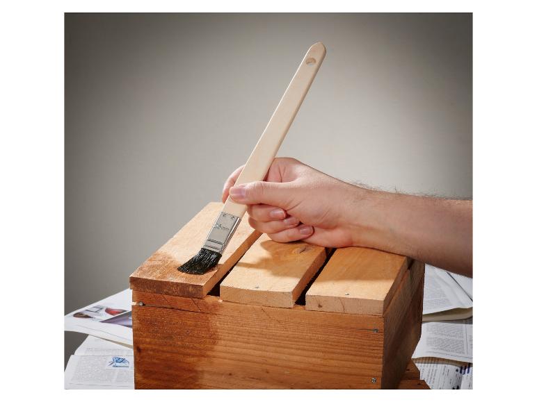 Main appliquant du vernis sur une caisse en bois avec un pinceau.