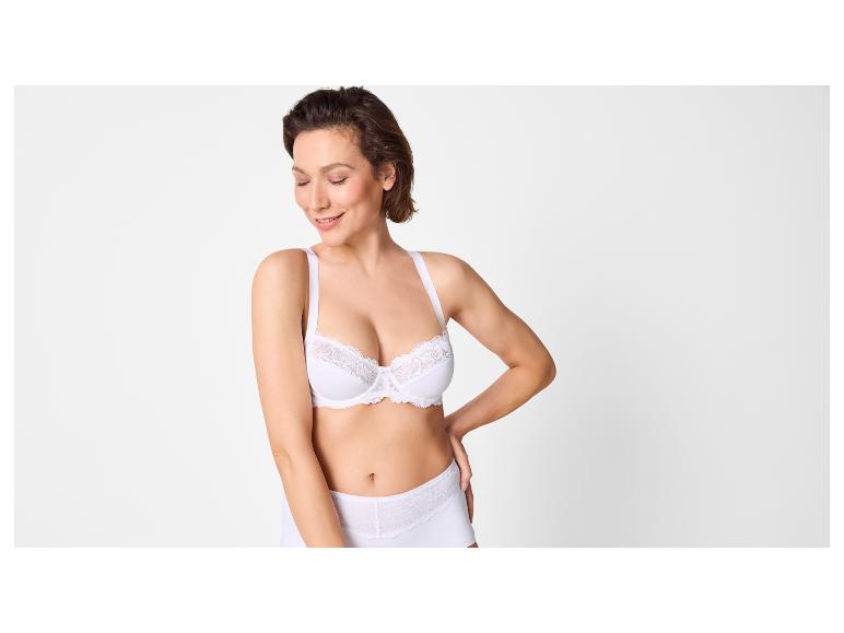 Femme en soutien-gorge et culotte blancs avec détails en dentelle, souriante.