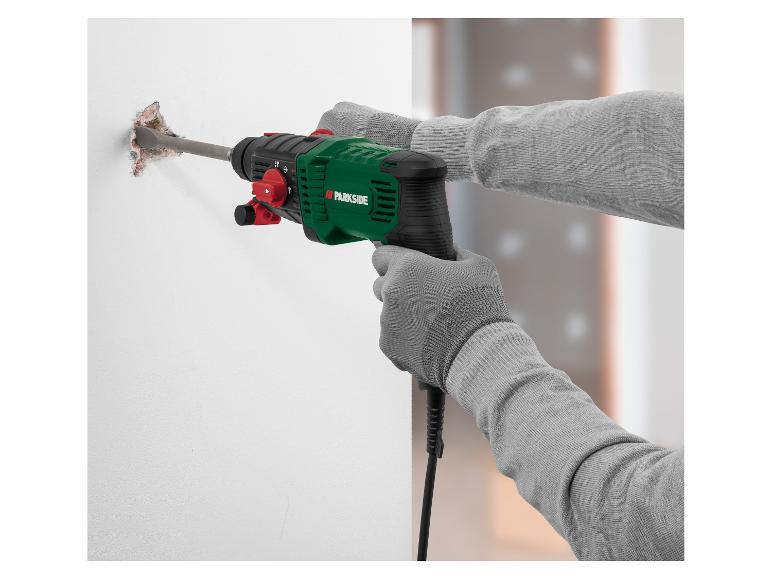 Un homme en gants gris utilise un marteau perforateur Parkside vert pour démolir un mur.